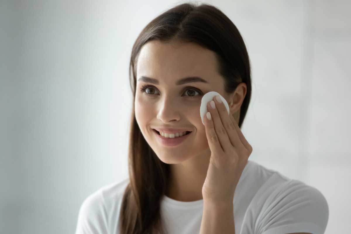 Smiling-millennial-girl-applying-toner-on-her-face